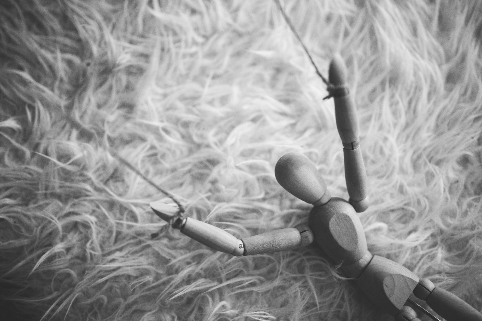 Image en noir et blanc d'une marionnette en bois posée sur une surface soyeuse, évoquant une ambiance dramatique et arti